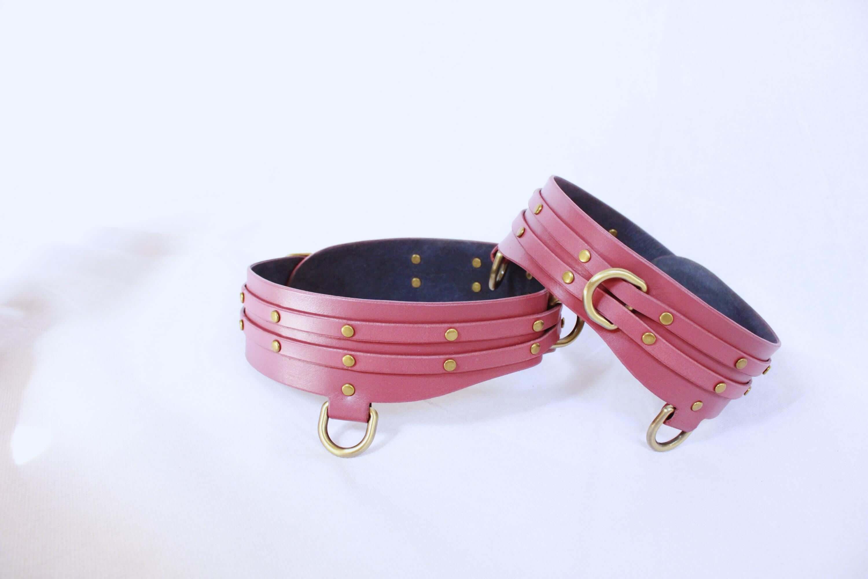Adjustable pink leather thigh cuffs set with gold studs, perfect for BDSM bondage gear and erotic play.