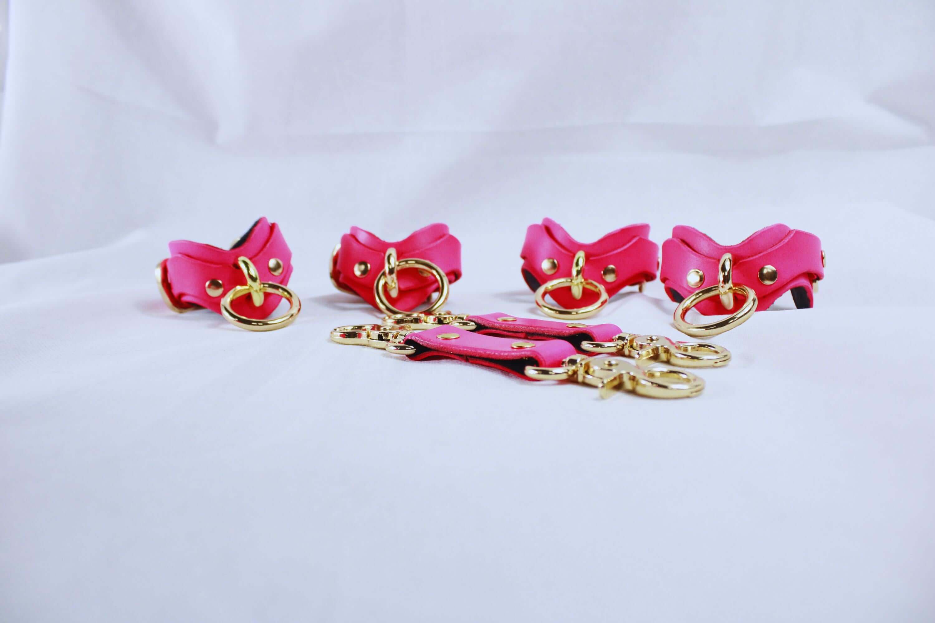 Pink leather BDSM bondage gear set with wrist and ankle cuffs, featuring gold metal hardware for a luxurious touch.