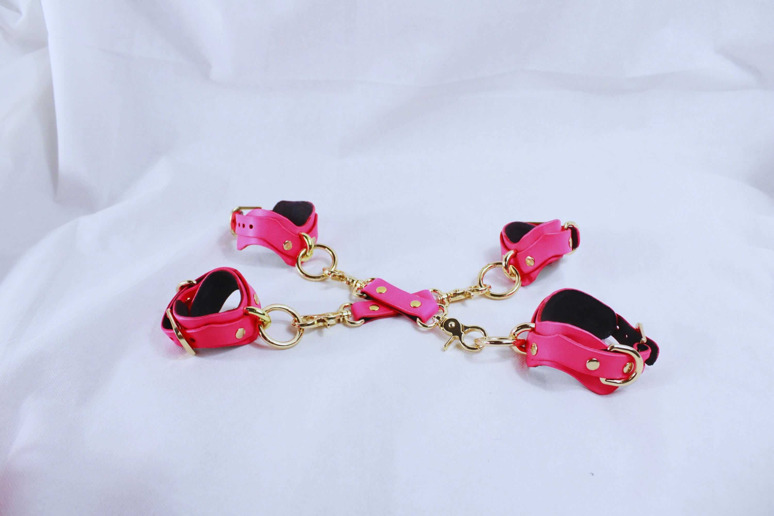 Pink leather BDSM bondage gear set with cuffs, gold hardware for submissive restraint and erotic play.