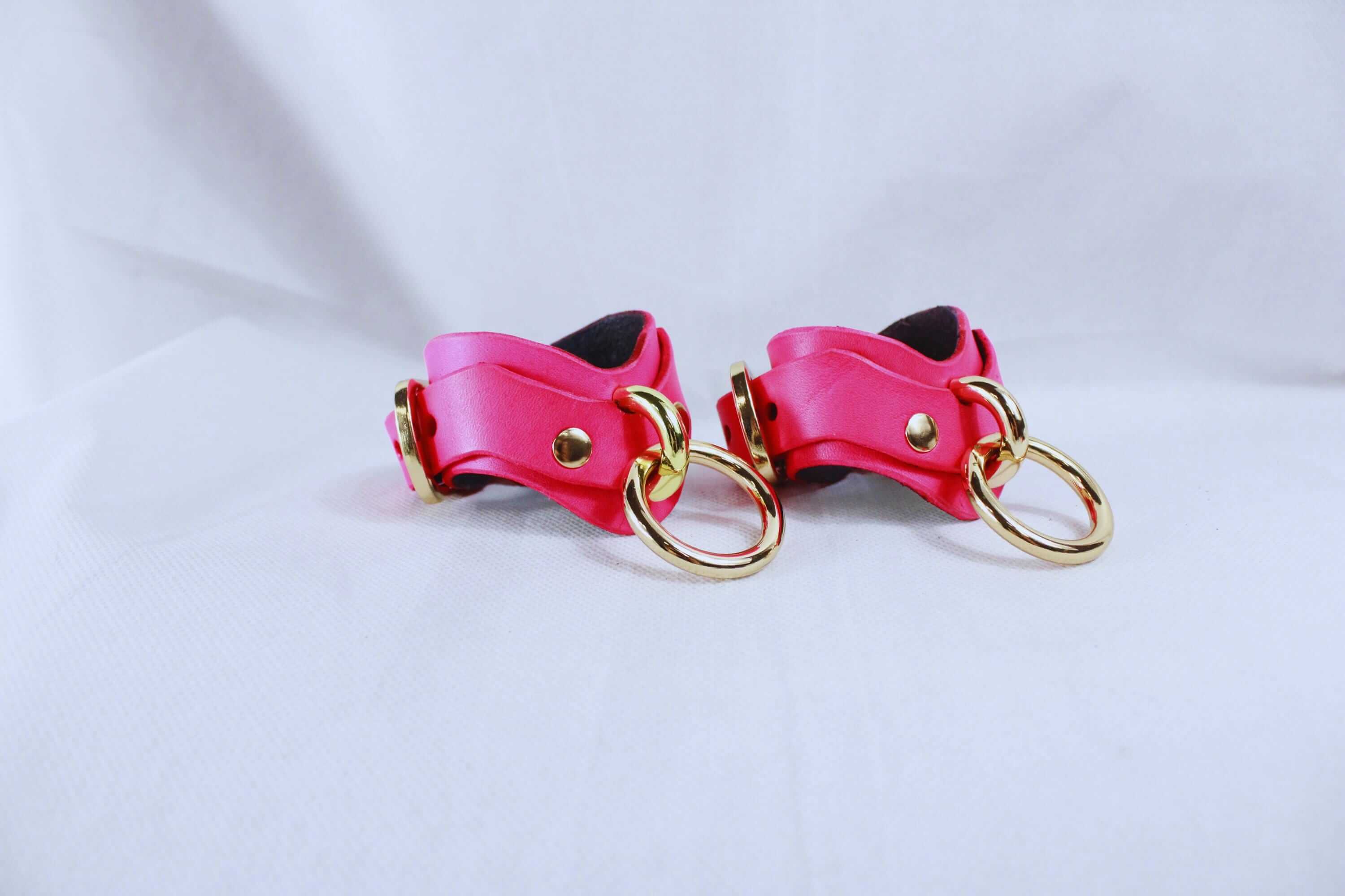 Pink leather wrist cuffs with golden hardware, part of a premium BDSM bondage gear set for submissive play.