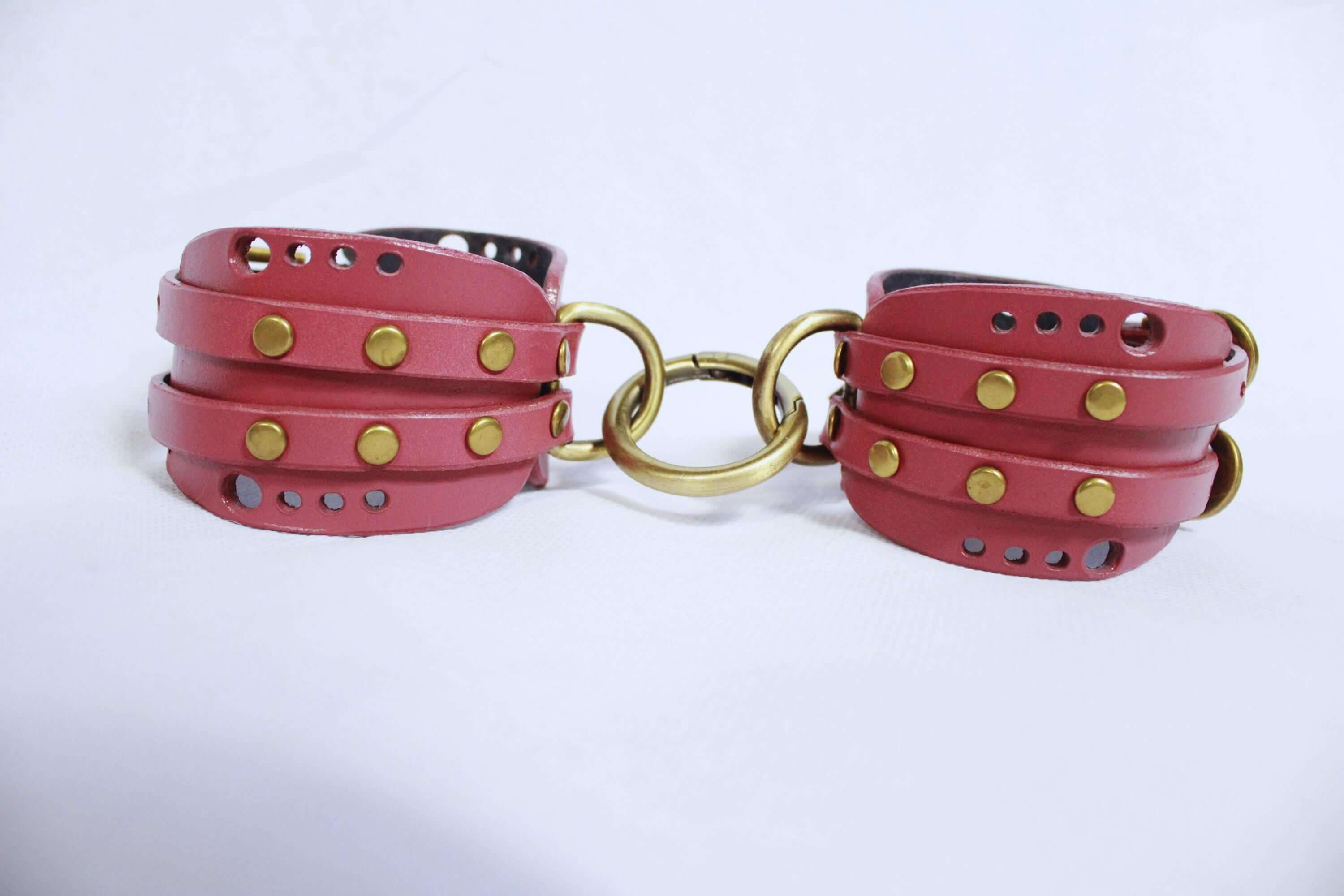 Mauve leather wrist cuffs with brass hardware for BDSM bondage play and submissive experiences.