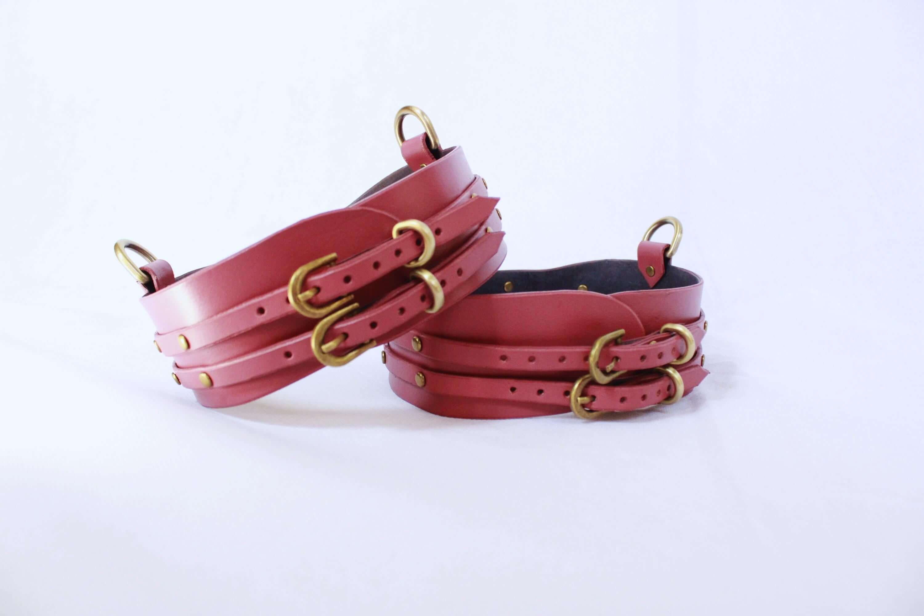 Adjustable leather thigh cuffs set with gold fittings, ideal bondage gear for submissives and enhanced play sessions.