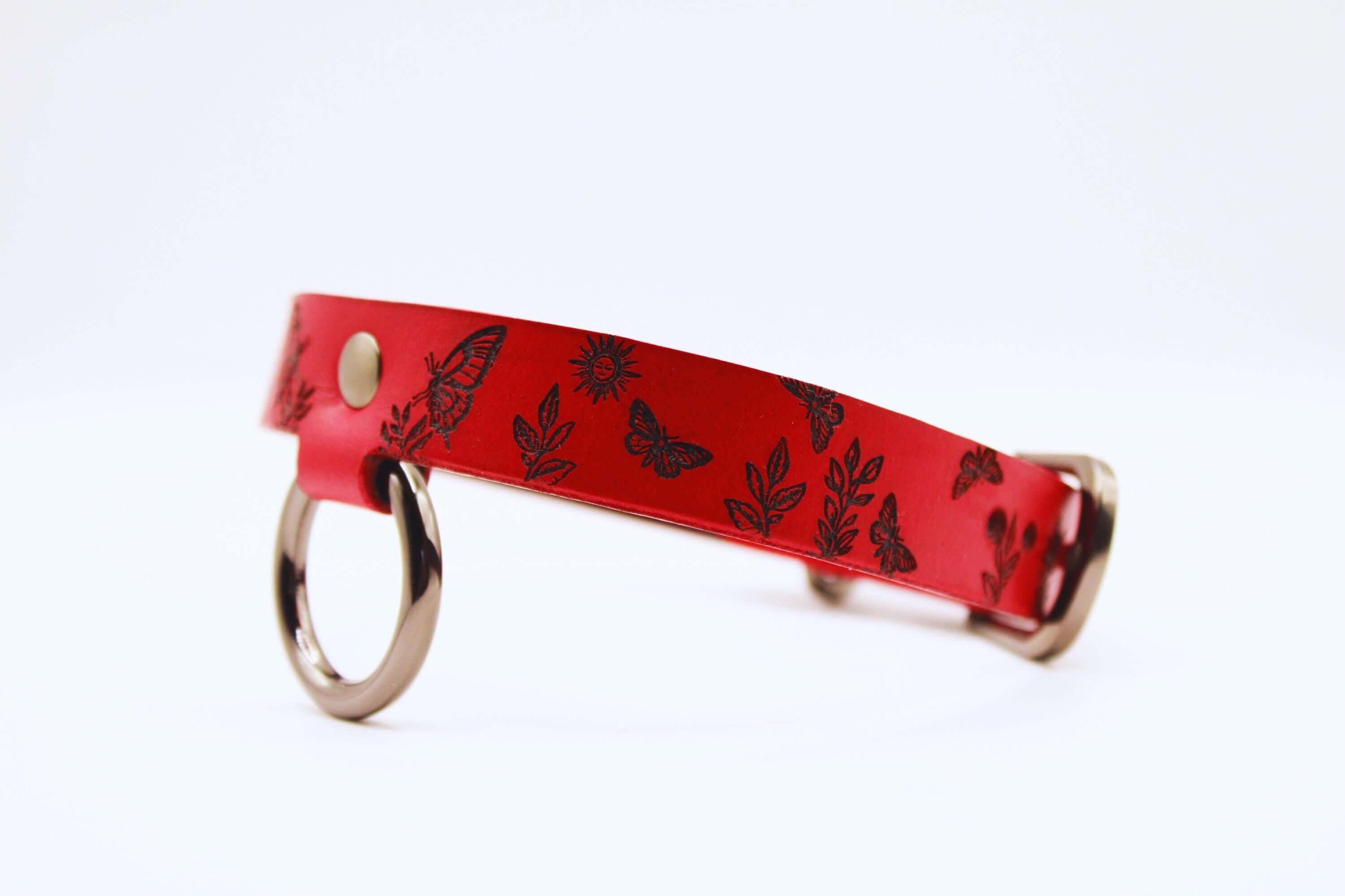 Discreet day collar handmade in red leather, featuring butterfly and sun designs. Ideal submissive collar for BDSM enthusiasts.