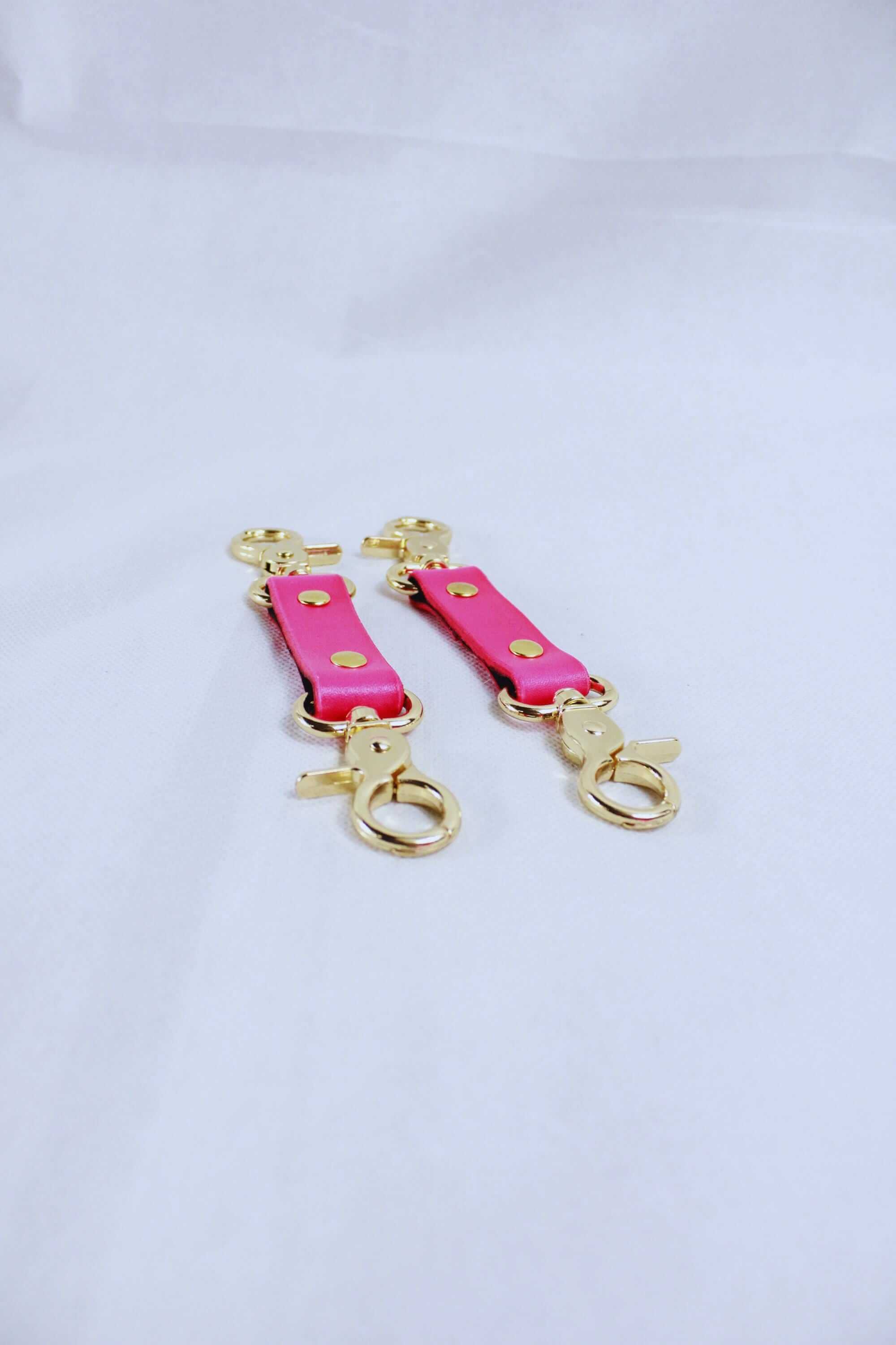 Pink leather wrist cuffs with golden hardware for BDSM bondage gear and submissive play.