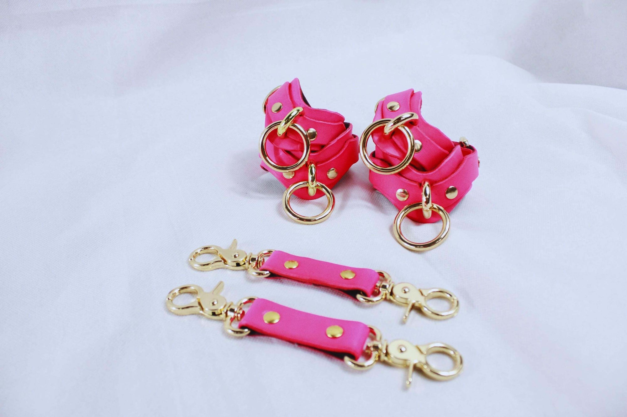 Pink leather wrist and ankle cuffs with gold hardware for BDSM bondage and submissive gear.