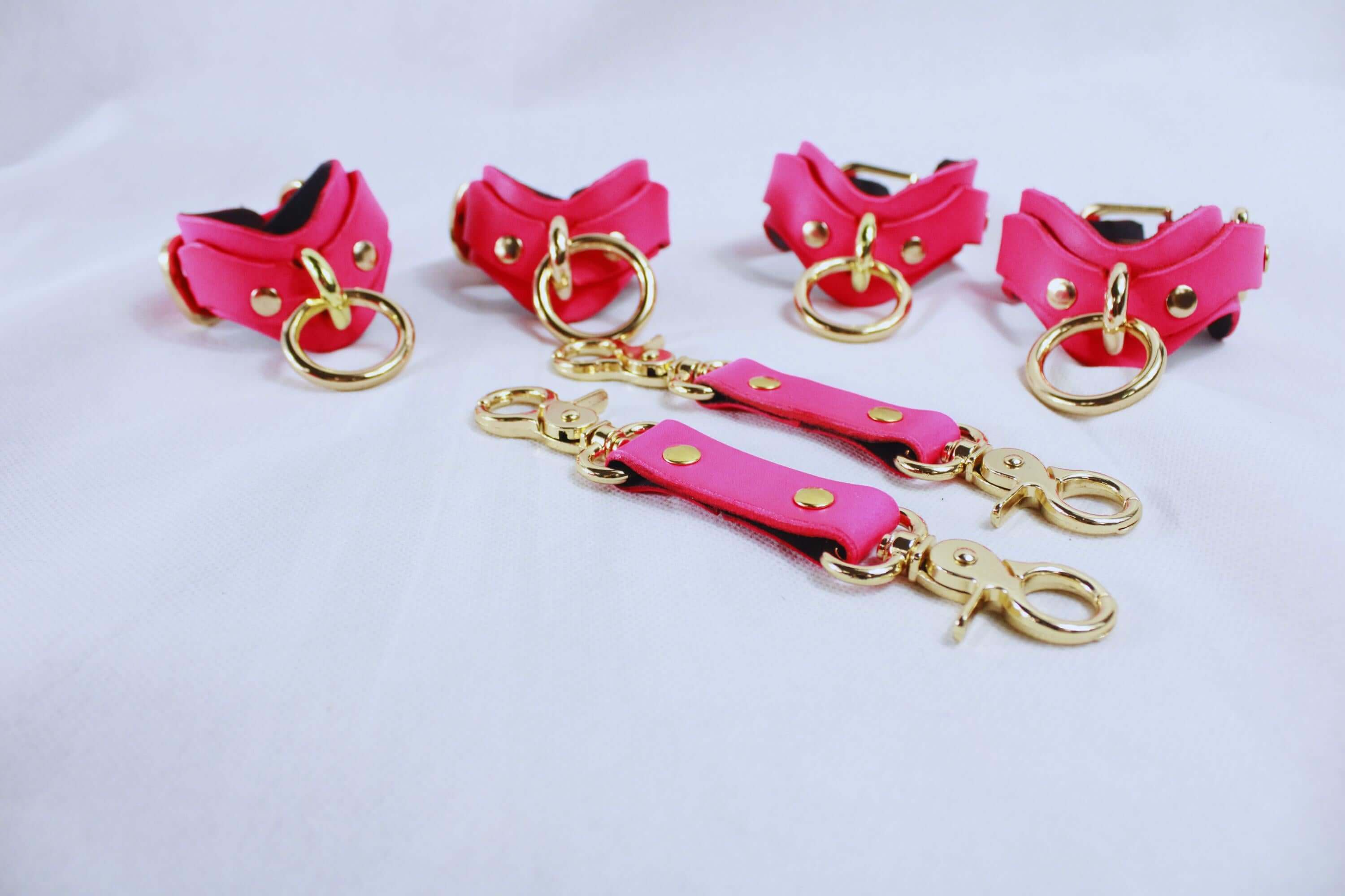 Pink leather BDSM bondage gear set with golden hardware, including wrist and ankle cuffs, perfect for submissive play.