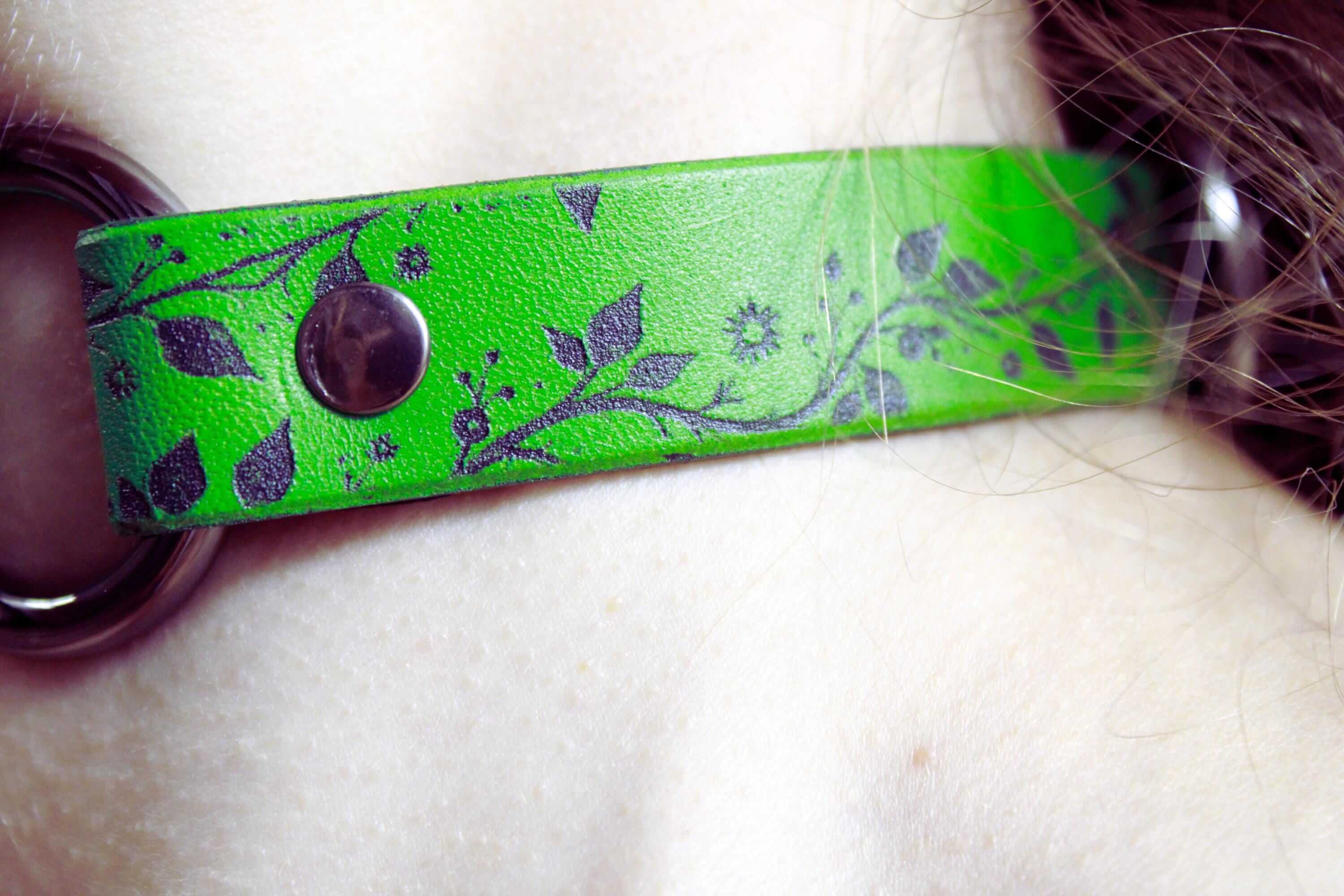 A close-up of a green leather strap with a floral pattern on it.