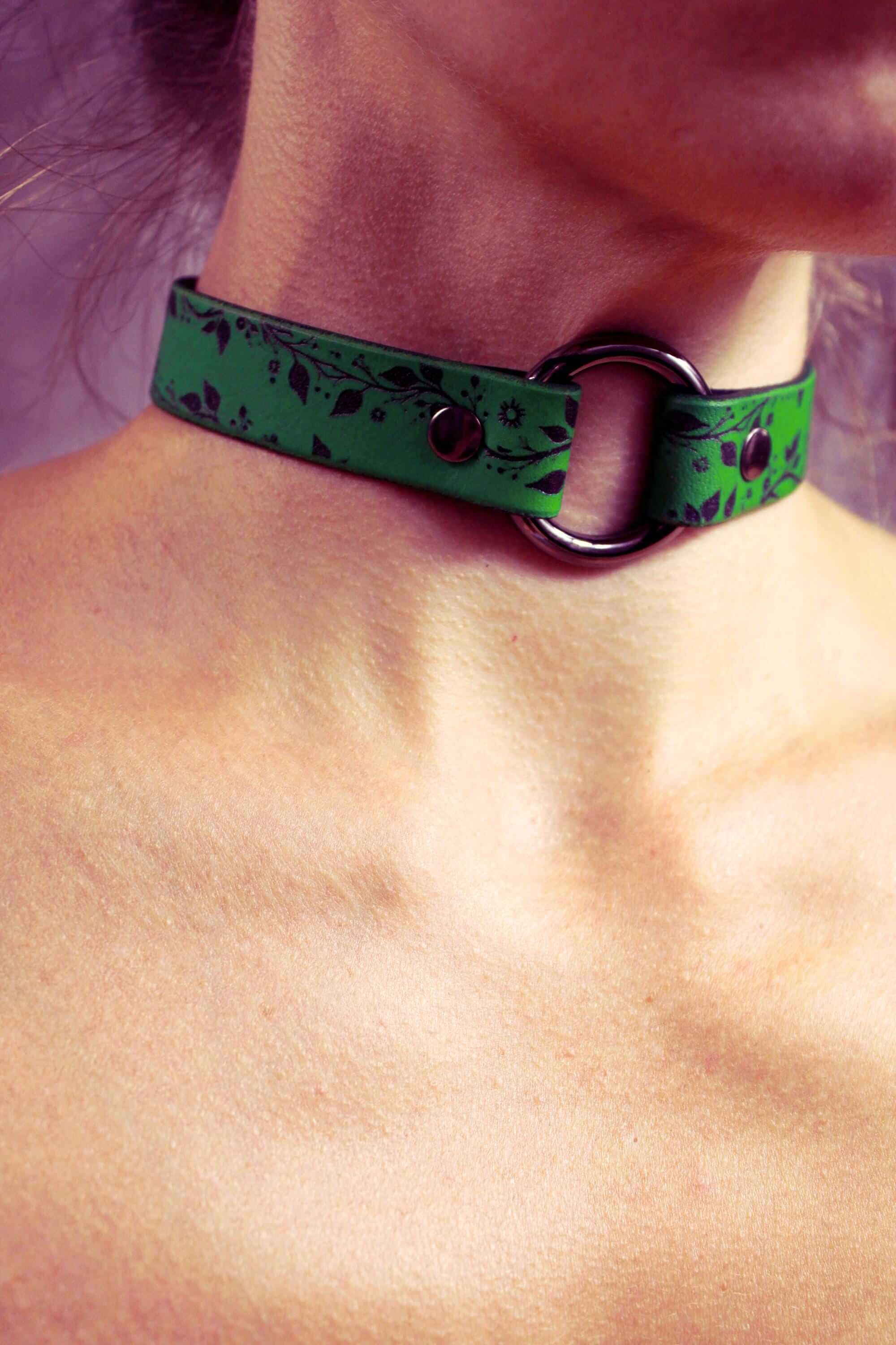 A close-up of a person's neck wearing a green choker necklace with a metal ring.