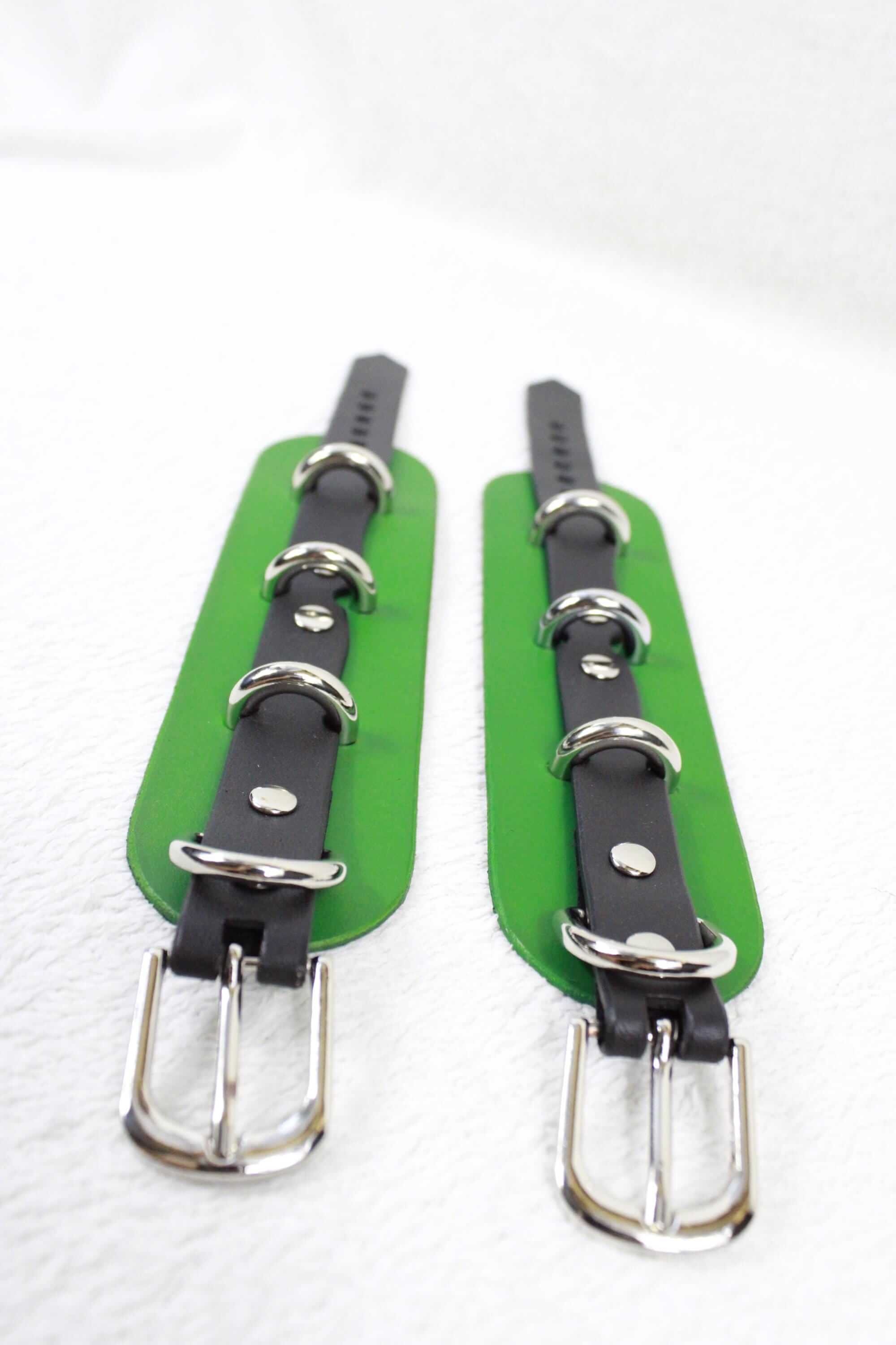 two green straps with black leather buckles, which appear to be designed for use with a leather belt.