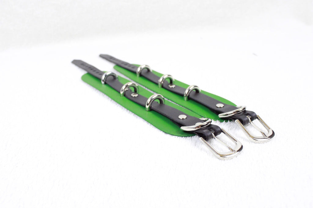 A pair of green leather straps with silver buckles, arranged diagonally on a white background.