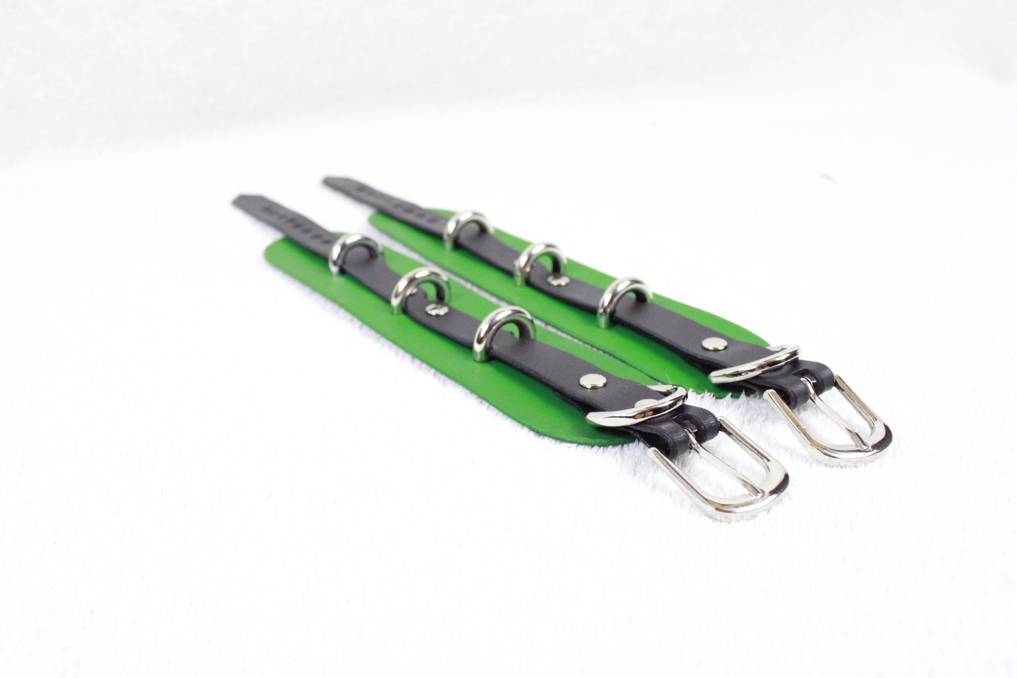 A pair of green leather straps with silver buckles, arranged diagonally on a white background.