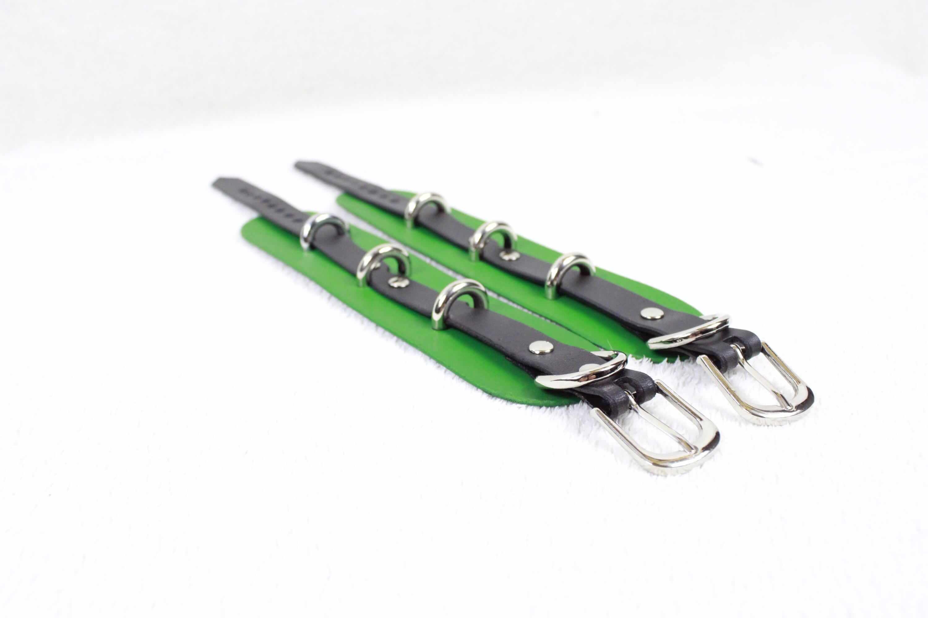A pair of green leather straps with silver buckles, arranged diagonally on a white background.