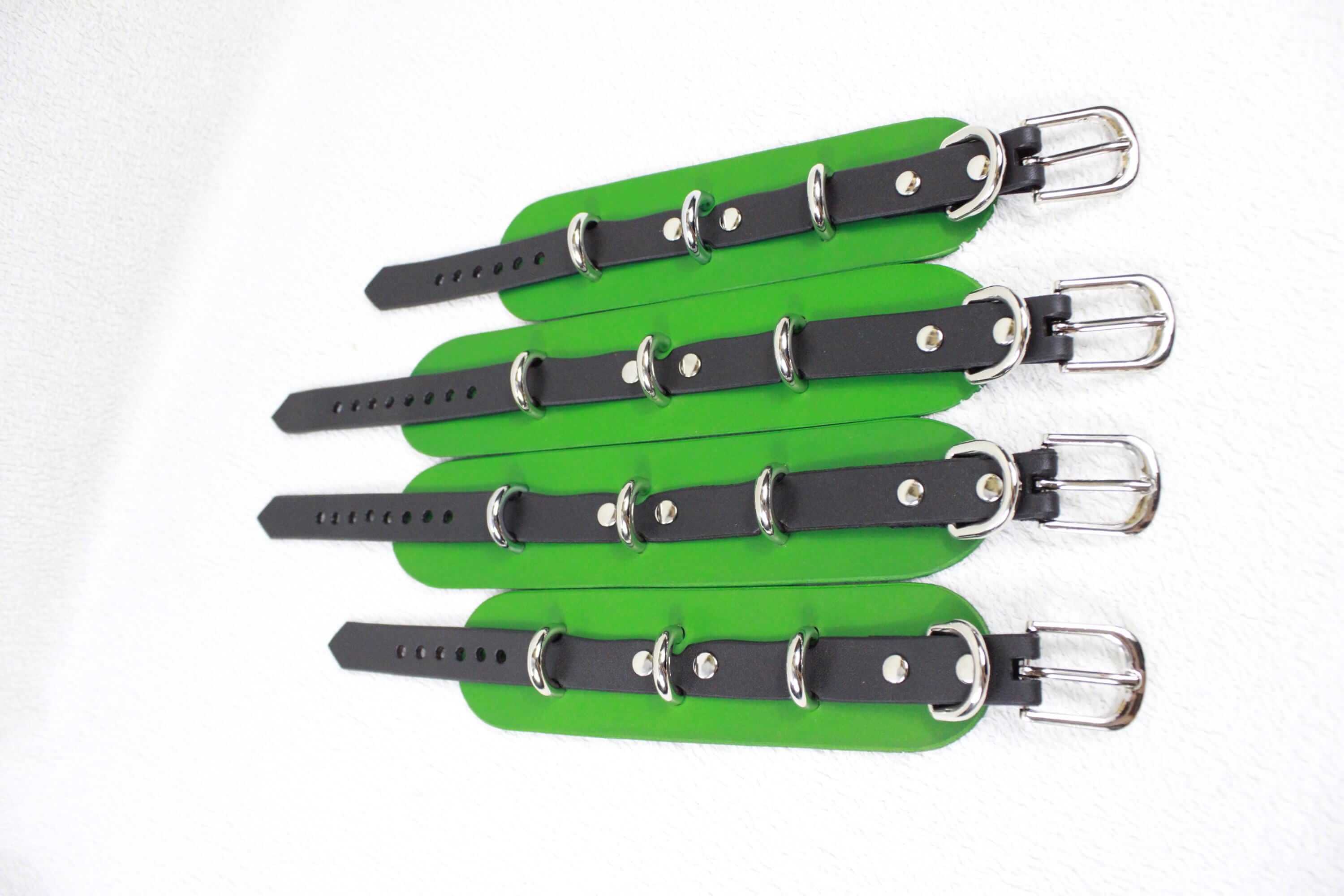 A group of green and black leather straps with silver buckles, arranged in a row.