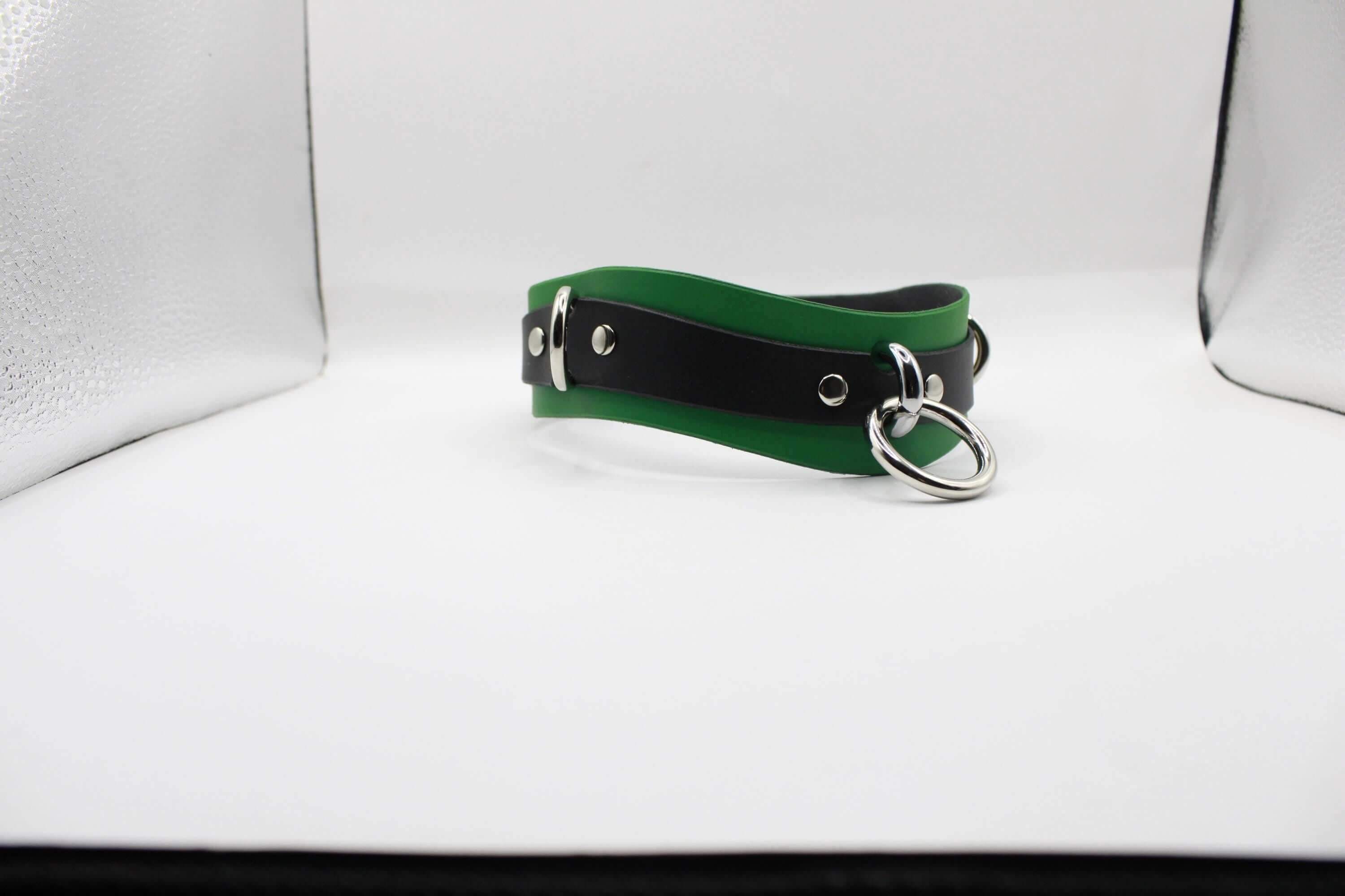 A green and black leather choker necklace with metal rings and a silver buckle is displayed against a white background.