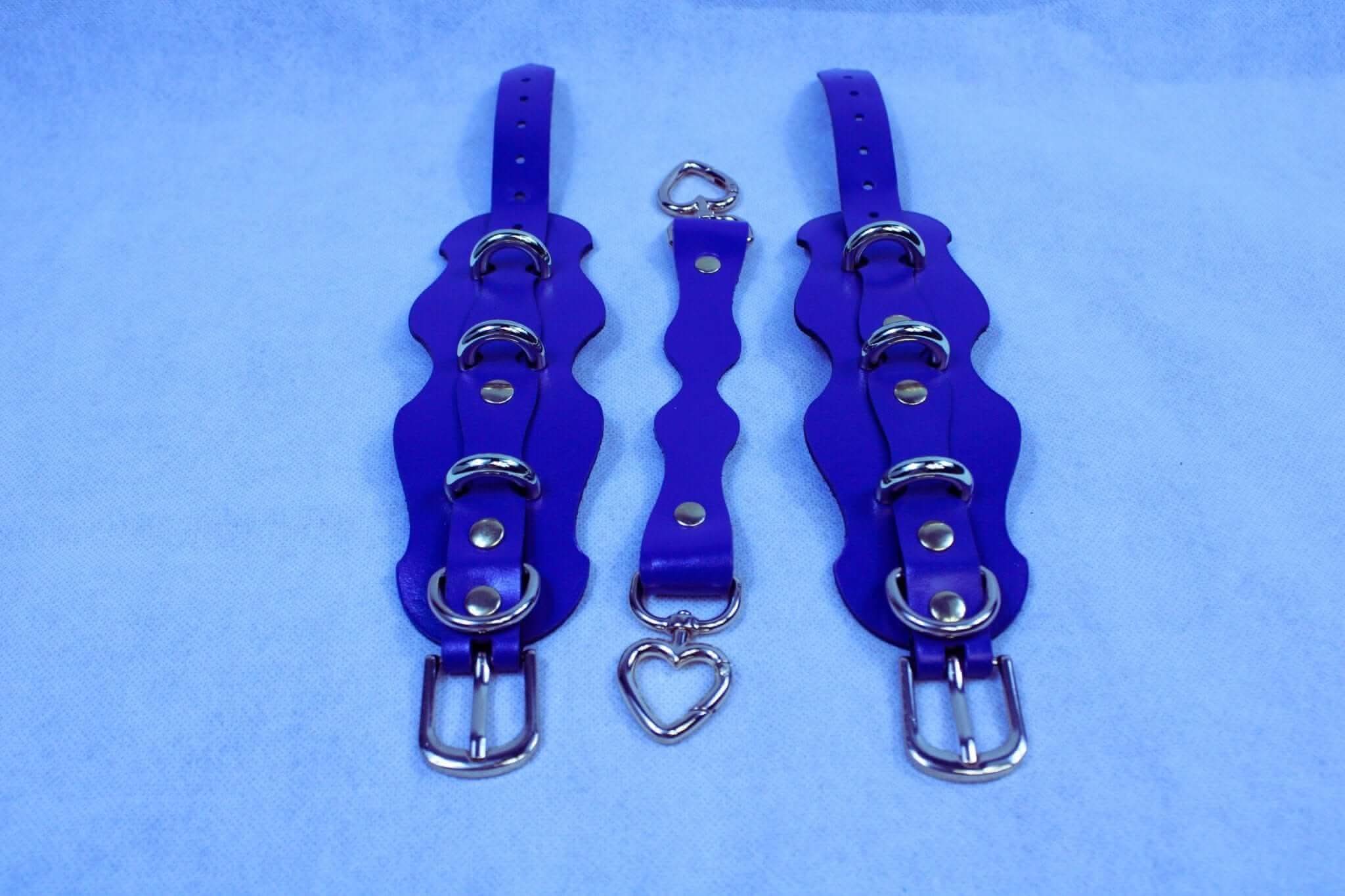 Purple handmade leather ankle cuffs with heart-shaped connector, ideal for bondage and D/s lifestyle accessories.