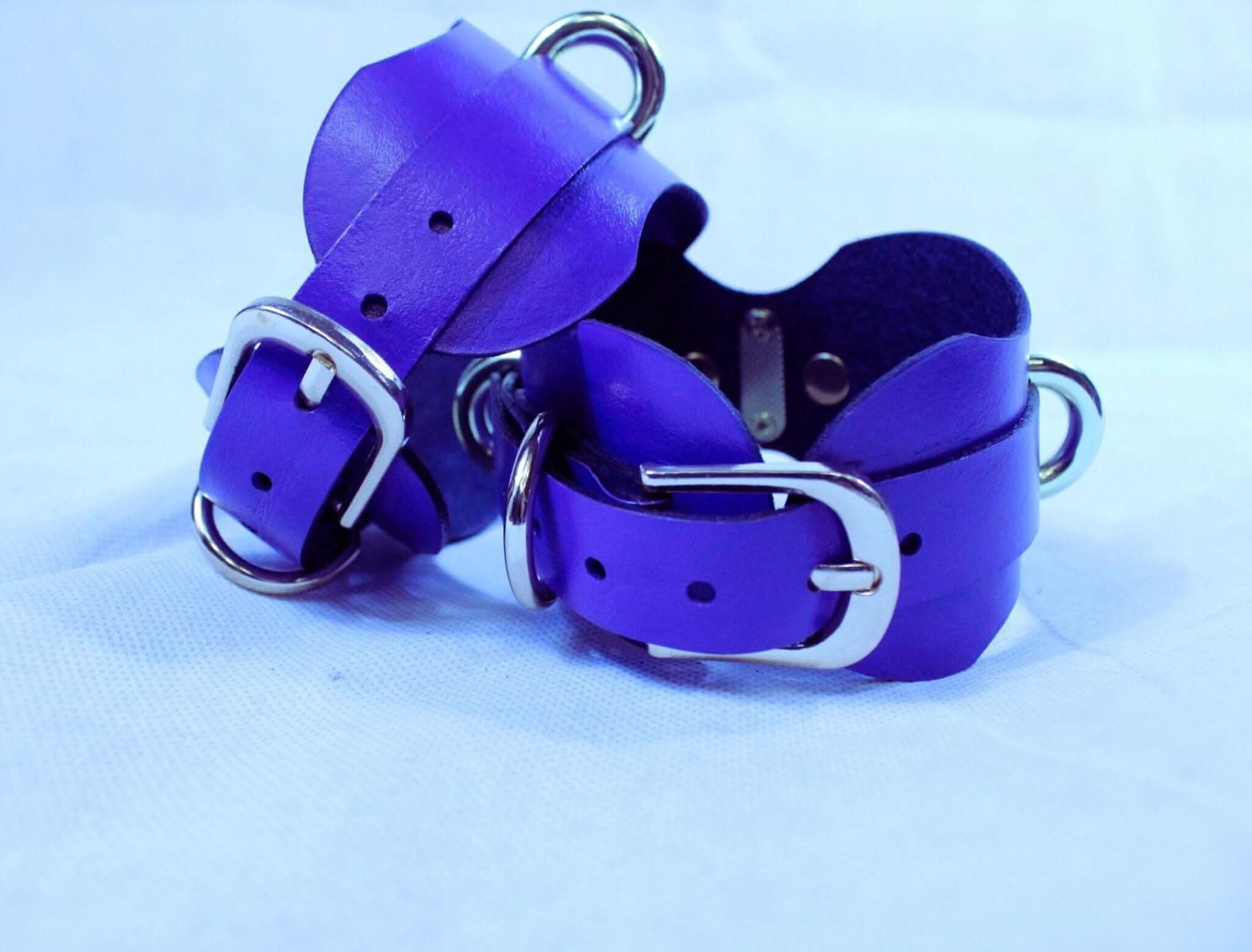 Purple leather ankle cuffs for bondage, adjustable restraint gear, perfect for BDSM and D/s lifestyle accessories.