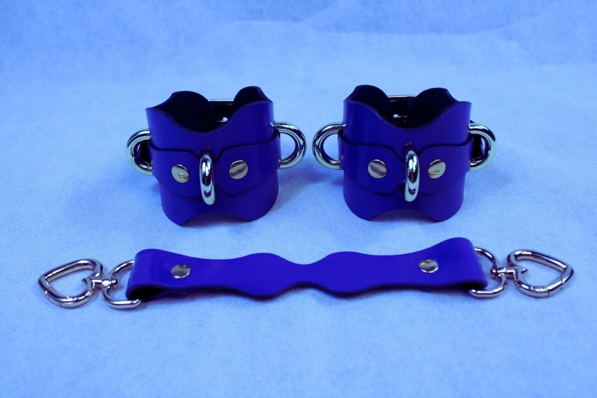Purple leather ankle cuffs with connecting strap, ideal for BDSM and bondage enthusiasts, offering comfort and adjustable restraint.