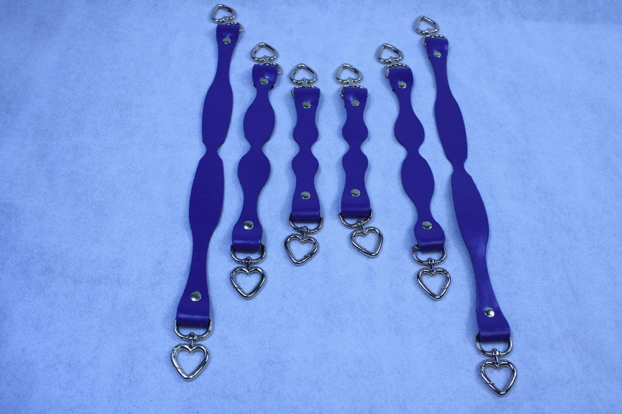 Handmade purple leather BDSM connectors with heart D-ring attachments, perfect for bondage gear and submissive accessories.