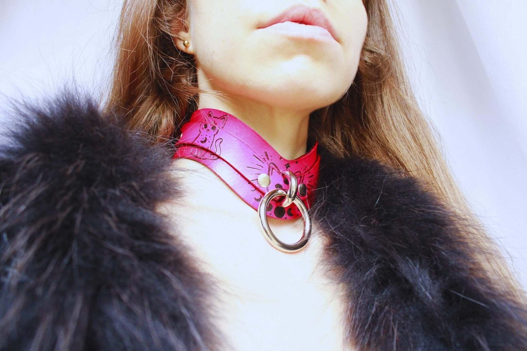 Close-up of a pink leather submissive day collar adorned with cat motifs and a metal ring, worn elegantly for BDSM style.