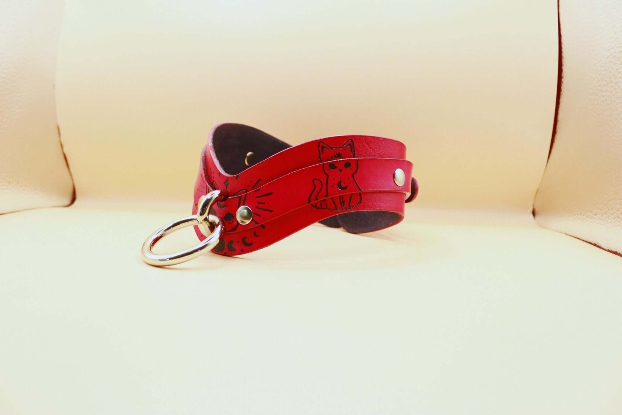 Elegant red leather submissive day collar with cat motifs, perfect for discreet BDSM wear and intimate play.