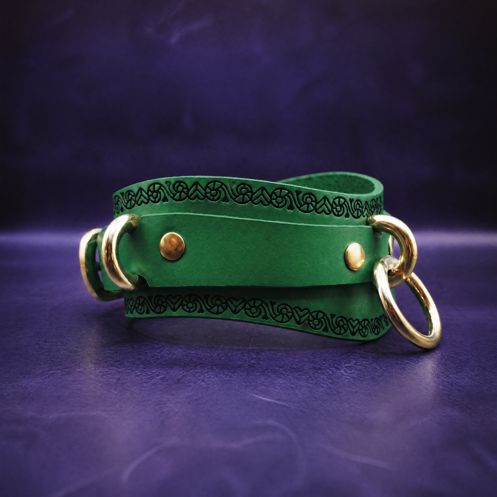 A green leather choker necklace with gold-colored metal rings and a decorative pattern on the front.