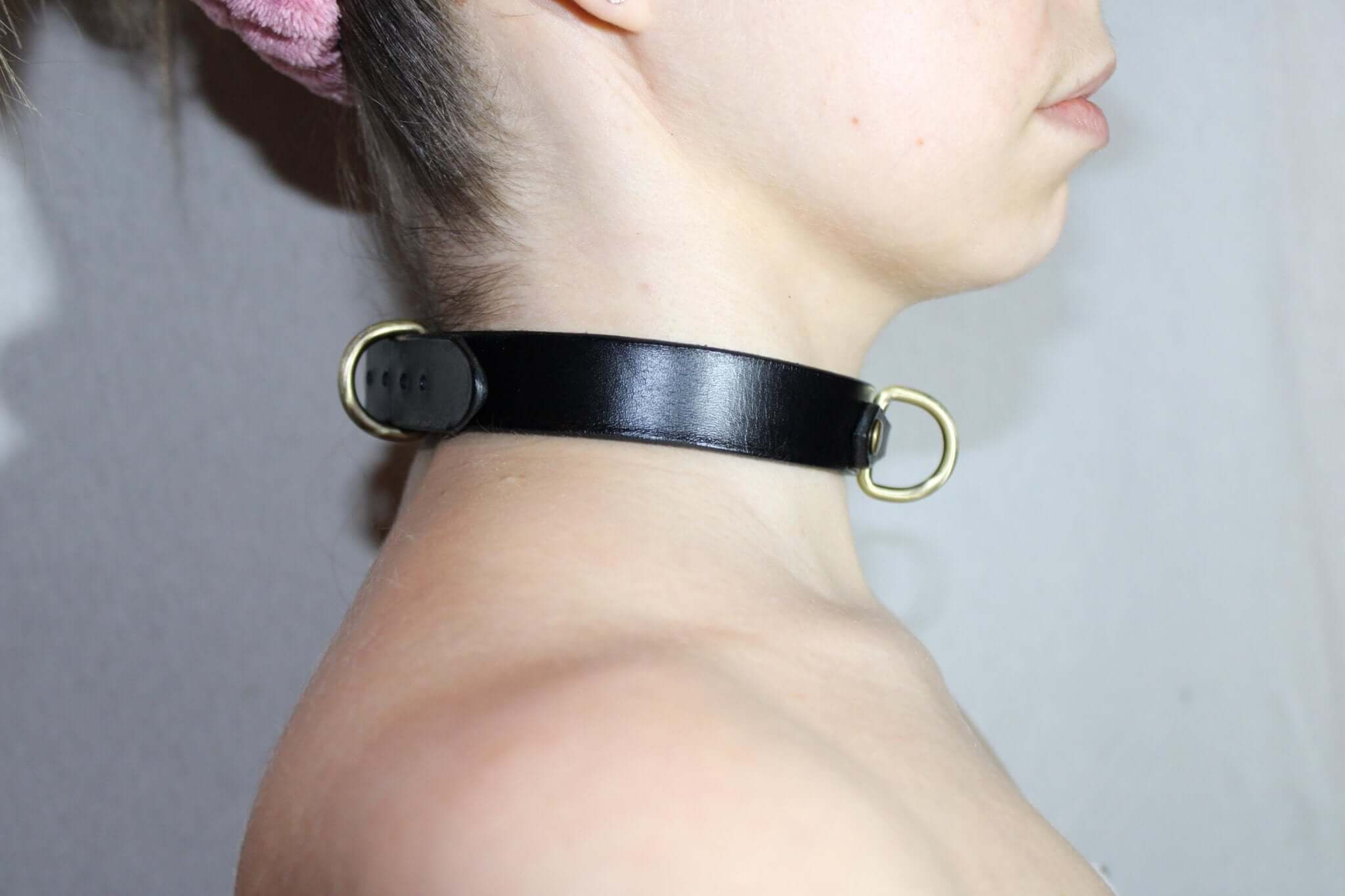 Minimalist black leather choker collar featuring gold rings, perfect for submissive jewelry and discreet day wear.