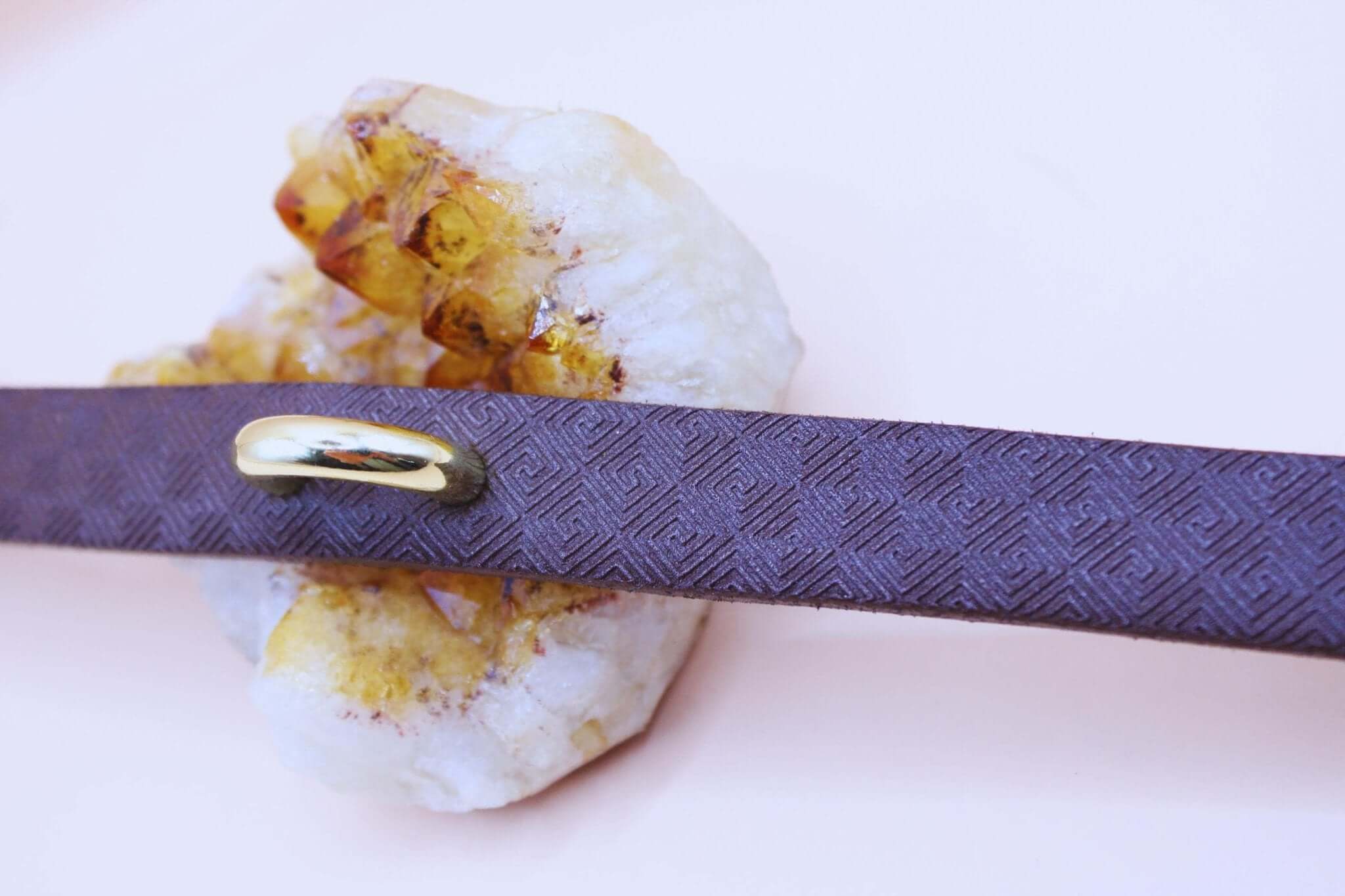 Elegant minimalist submissive collar with gold accent on textured dark brown leather, styled on a crystal backdrop.