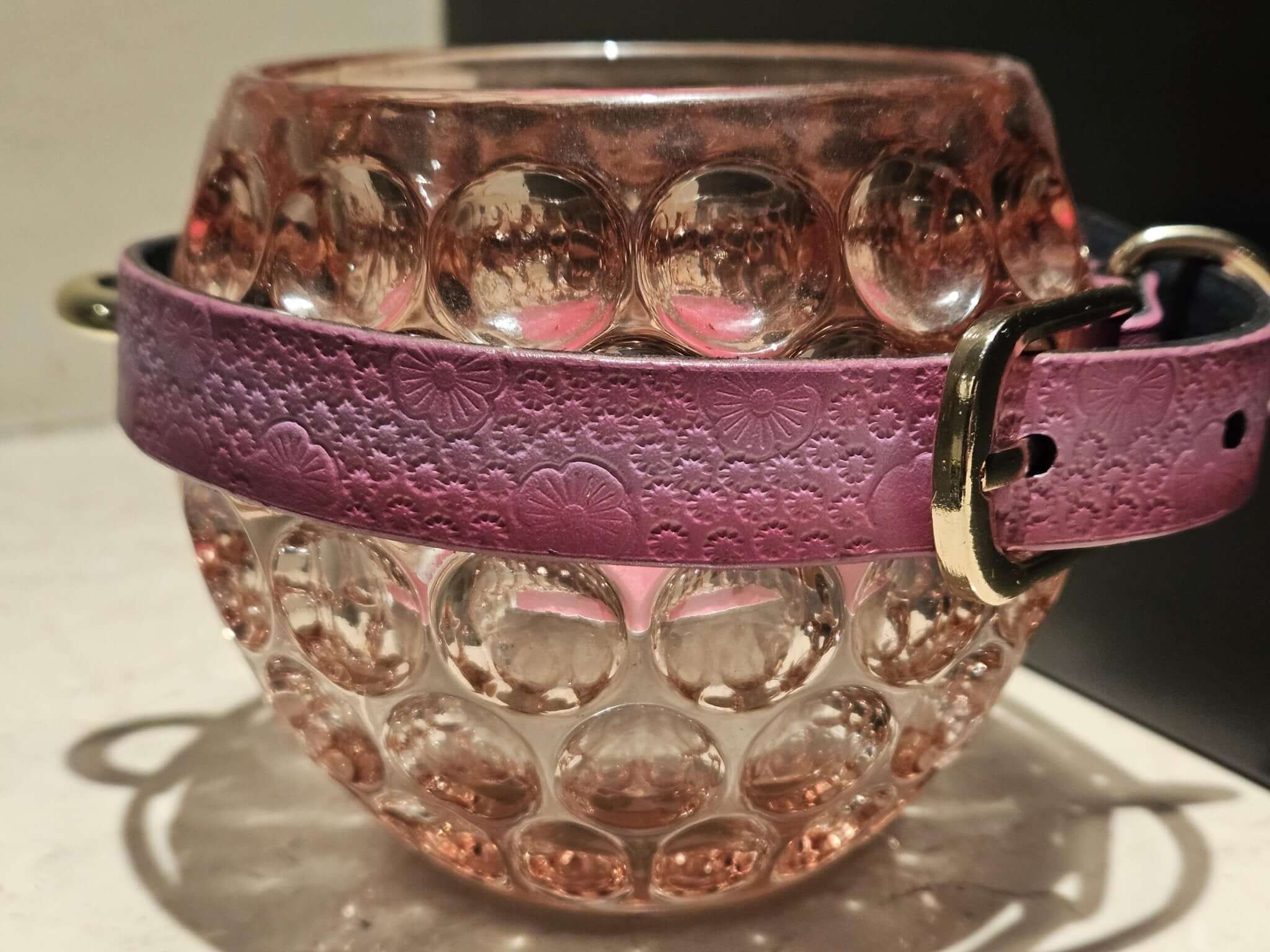 Pink floral embossed leather collar wrapped around a glass decorative piece, showcasing elegant bdsm design and aesthetics.