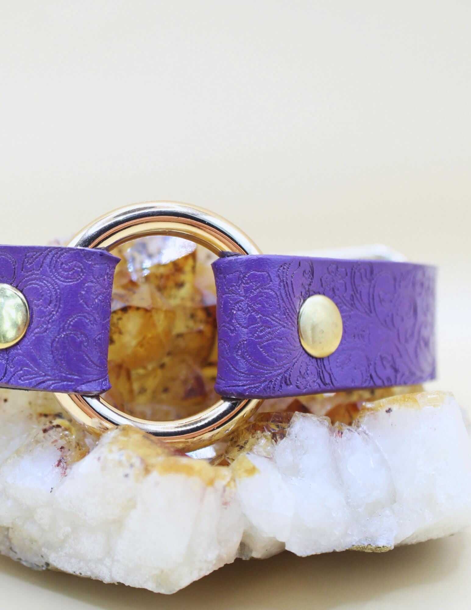 Purple leather BDSM collar with floral embossing and central O-ring, ideal for submissive jewelry and bondage gear.