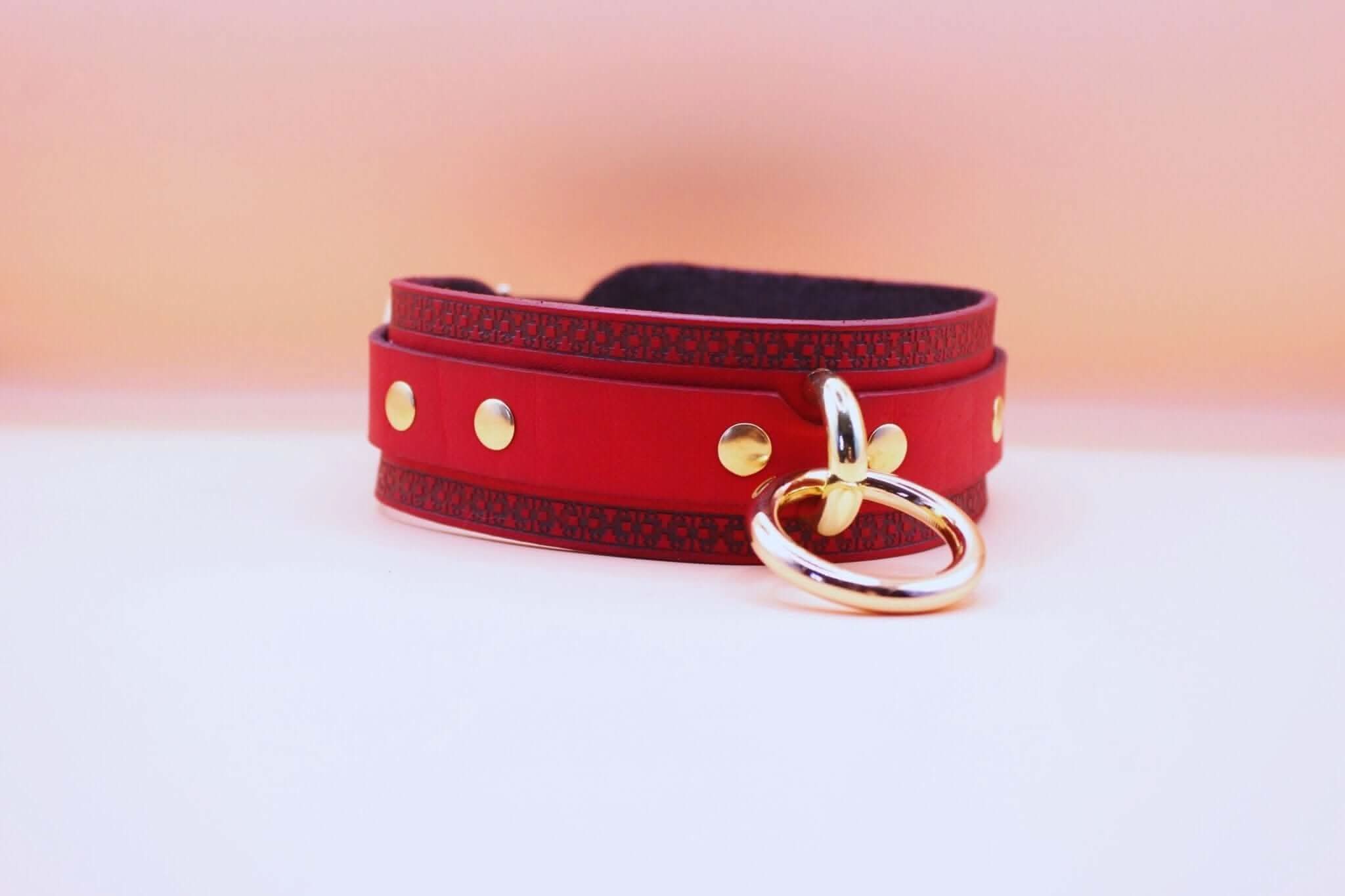 Red bondage collar with gold ring, a stylish submissive necklace for elegant BDSM play.