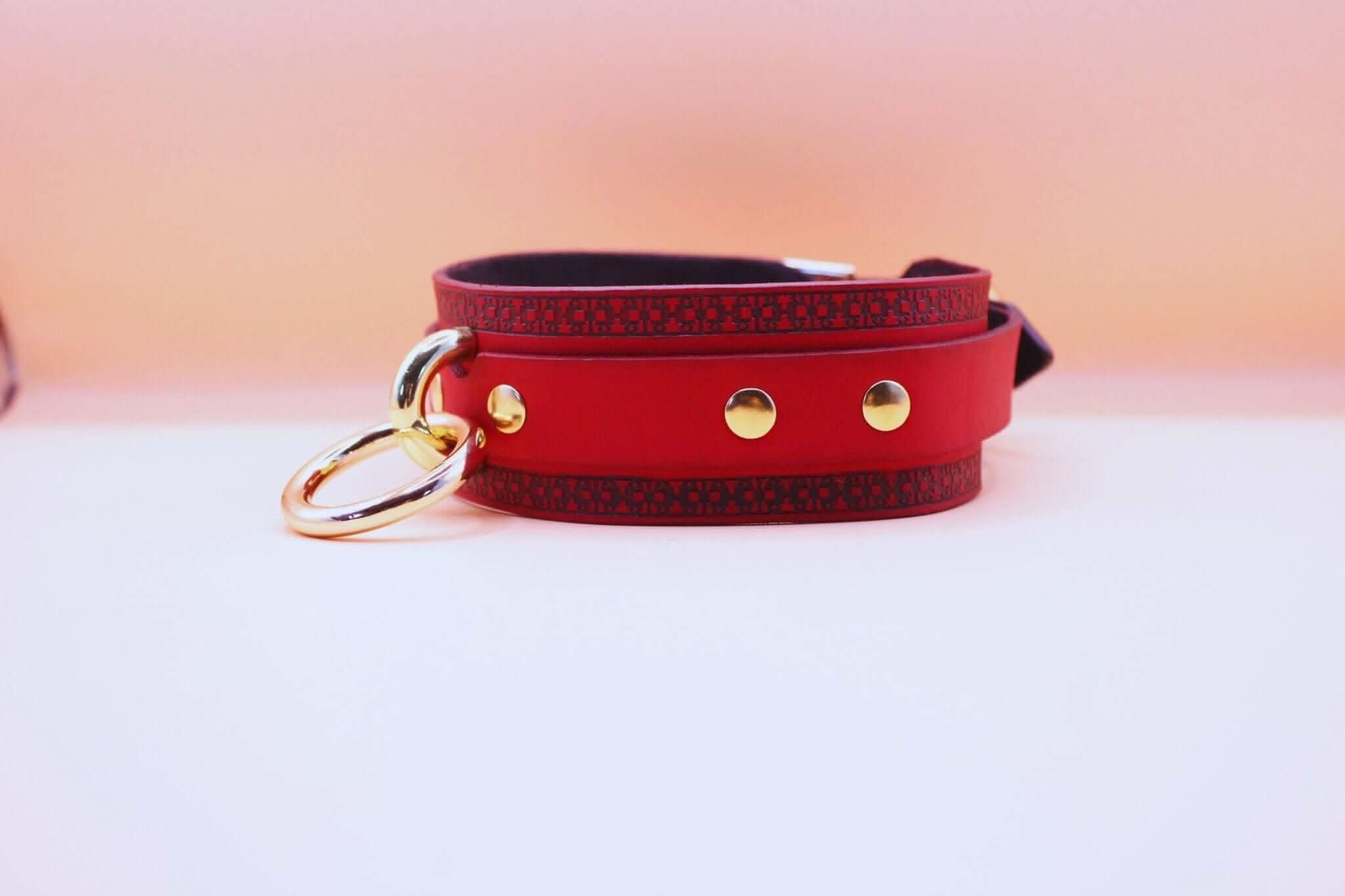 Red bondage collar with golden ring, ideal for submissive jewelry and BDSM play, featuring intricate black engraving.
