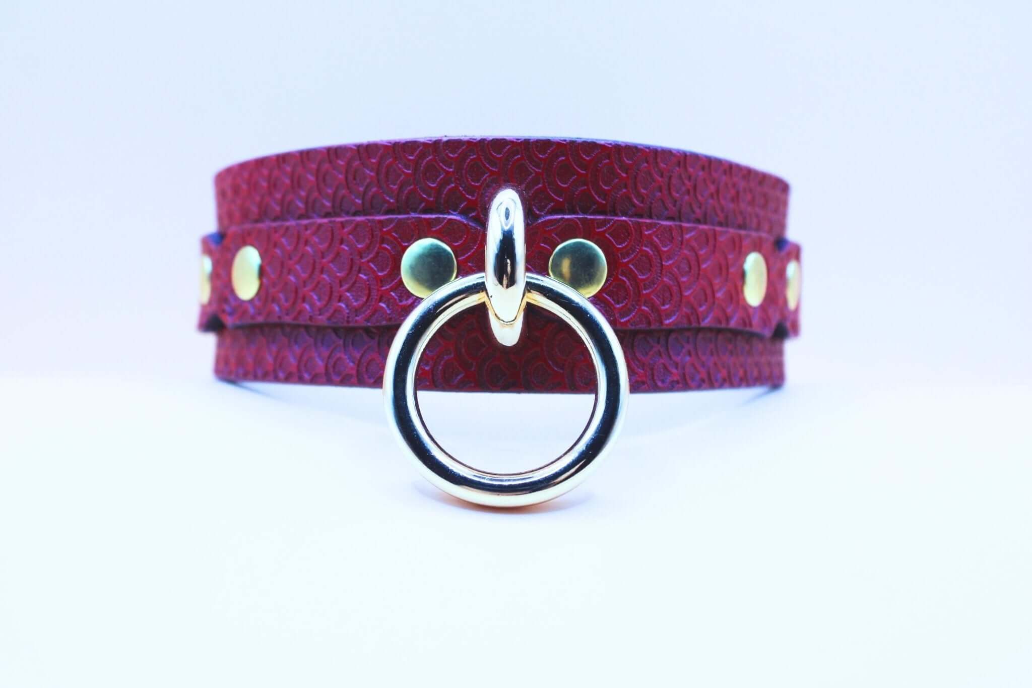 Red leather BDSM collar with embossed pattern and silver O-ring, perfect for submissive jewelry and bondage gear.