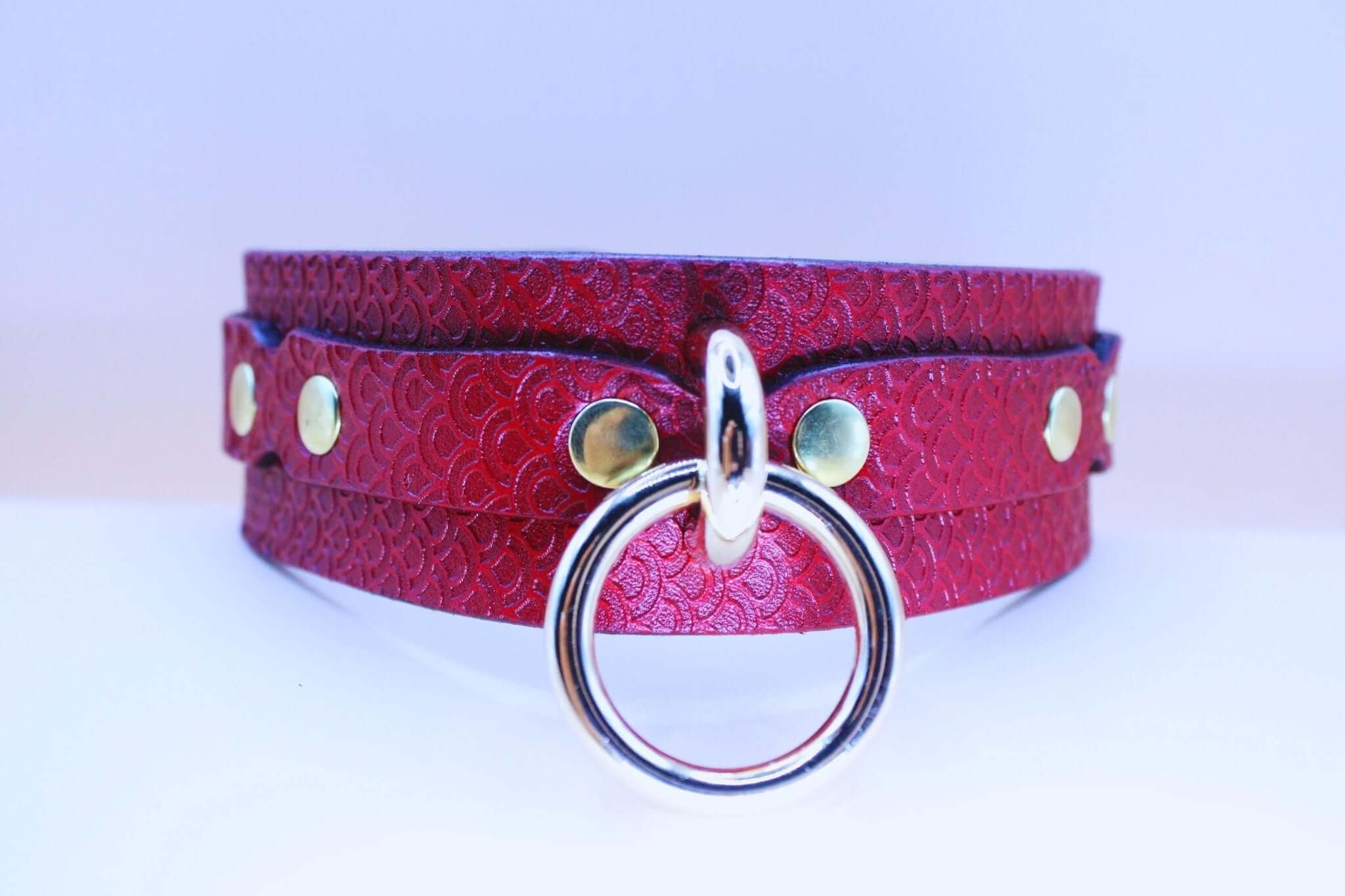 Deep red leather submissive collar with embossed pattern and large silver O-ring, perfect for BDSM and erotic wear.