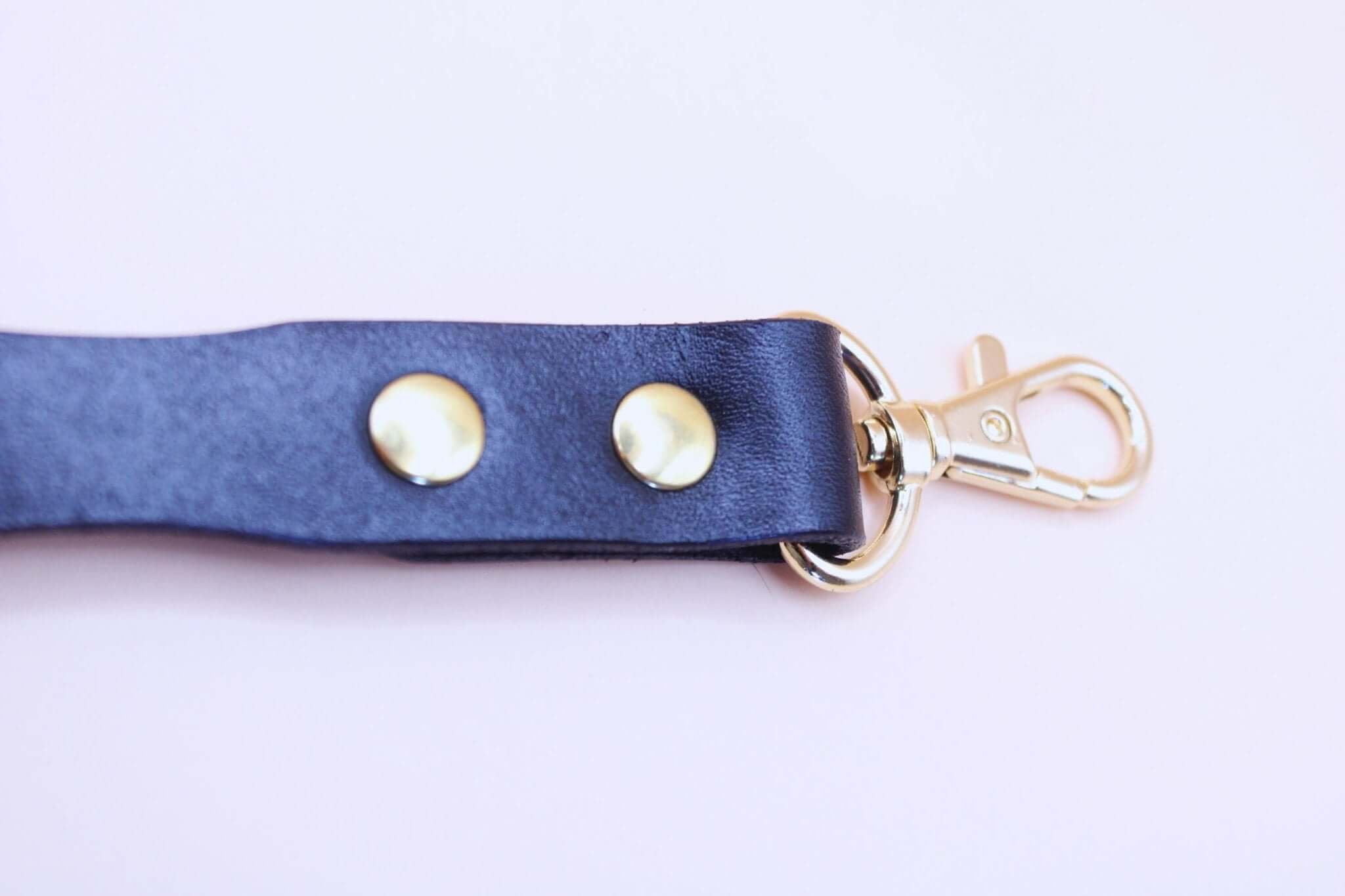 Close-up of a short black leather BDSM leash with gold hardware, perfect for submissive control and bondage gear.