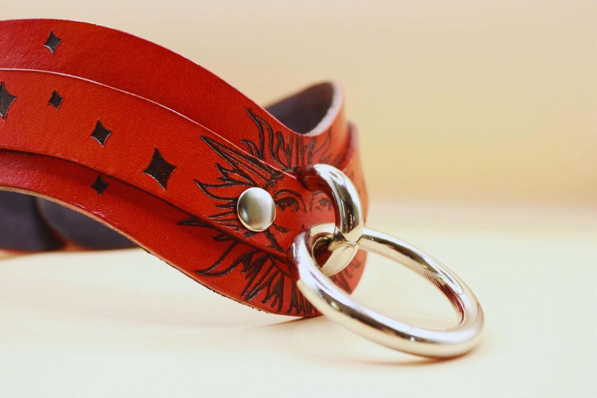 Sun Design BDSM collar in red leather, featuring a ring and intricate sun pattern, ideal for discreet sub jewelry.