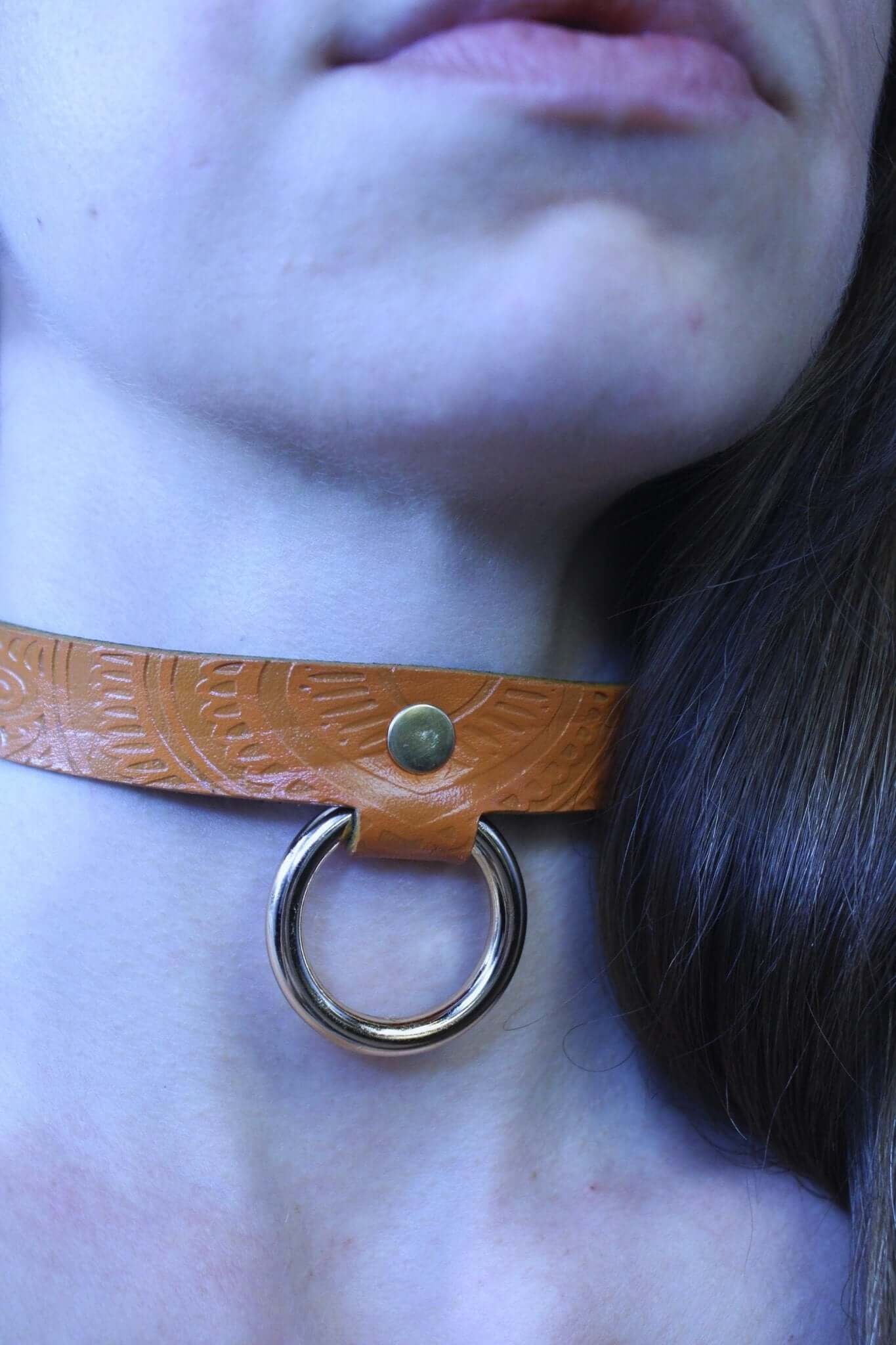 Tan leather BDSM collar with embossed patterns and metallic ring, perfect for submissive jewelry and stylish bondage wear.