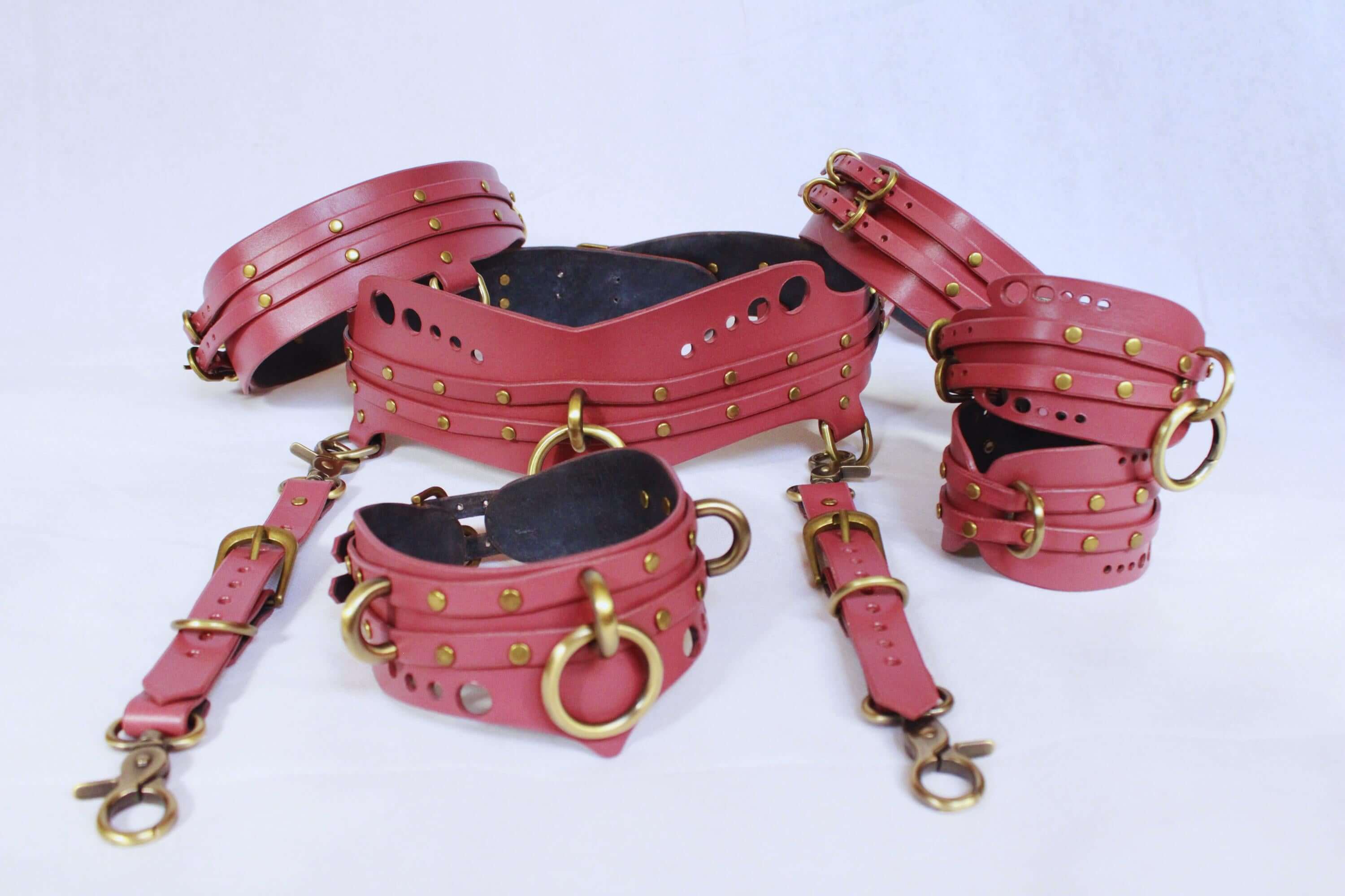 Bondage harness set including thigh cuffs, submissive collar, and wrist restraints in mauve with golden hardware for BDSM.