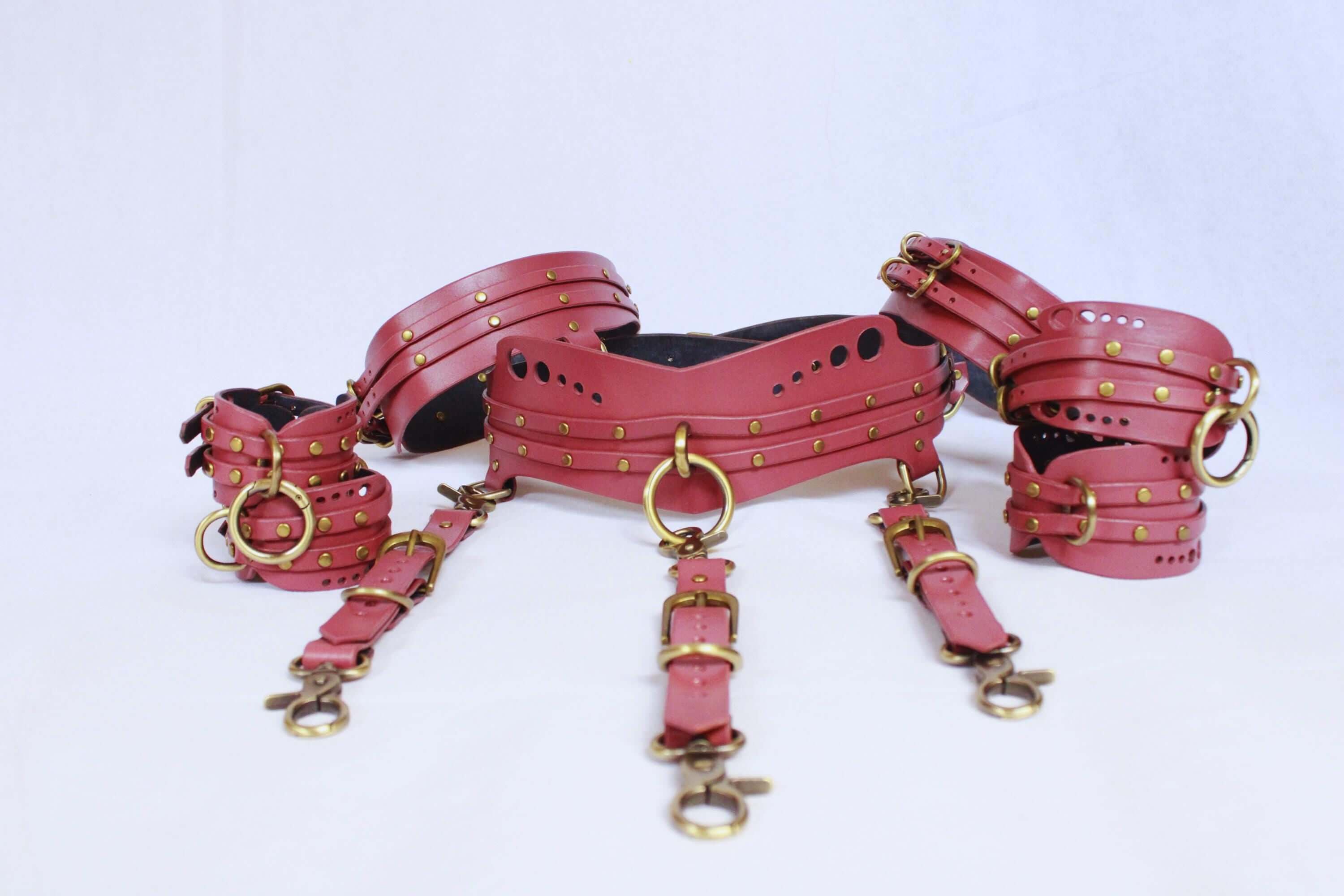 Leather bondage harness set in mauve with gold hardware, includes thigh cuffs, garter belt, and wrist restraints for BDSM lovers.
